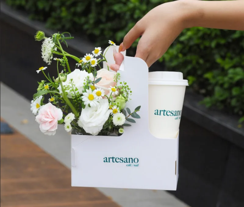 Picture of a package from Artesano Cafe and Nail featuring their drinks, a flower, and the nails of the person holding the package